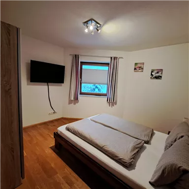 A cozy bedroom with a double bed and bright walls. A television and a window provide pleasant light.