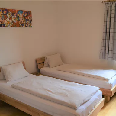 A simple room with two single beds and a window that looks out on a green meadow. A decorative picture hangs on the wall.