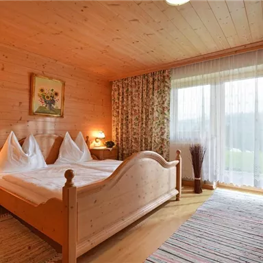 Ein gemütliches Schlafzimmer mit Holzverkleidung und einem großen Fenster. Es gibt ein Doppelbett und hübsche Blumenvorhänge.