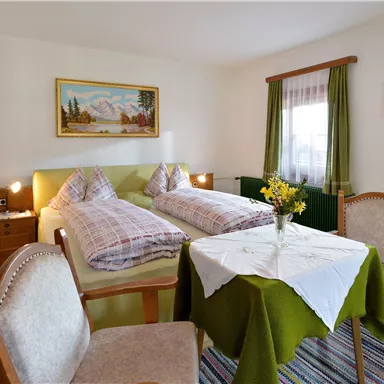 A cozy room with two beds and a table. There are chairs and a beautiful decoration on the walls.
