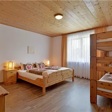 A cozy bedroom with wooden furniture and two beds. The room has plenty of daylight and a warm atmosphere.