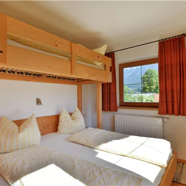 A cozy bedroom with a bunk bed and a double bed. Large windows provide plenty of daylight and a view of the outdoors.