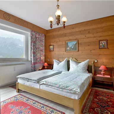 Ein gemütliches Schlafzimmer mit Holzwänden und einem großen Bett. Die Dekoration umfasst farbige Vorhänge, eine Teppich und schöne Bilder an der Wand.