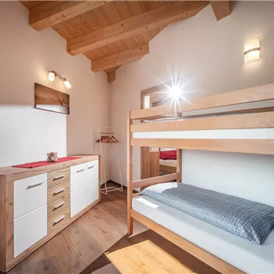Ein gemütliches Schlafzimmer mit einem Holzbunkbett und modernen Möbeln. Große Fenster sorgen für viel Licht und eine warme Atmosphäre.