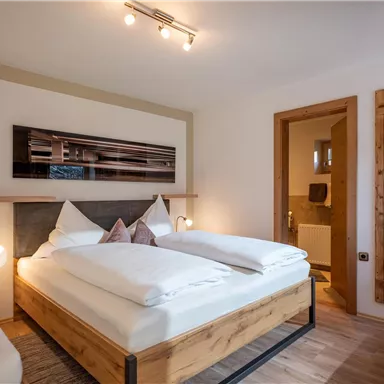 Ein modernes Zimmer mit einem Doppelbett und gemütlicher Einrichtung. Der Raum verfügt über Holzdetails und eine angenehme Beleuchtung.