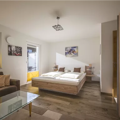 A modern bedroom with a large bed and bright wooden flooring. The rooms are well-lit and furnished in a minimalist style.