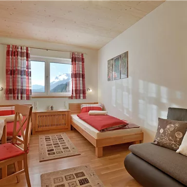 Ein gemütlicher Raum mit einem Einzelbett, einem Sofa und einem Esstisch. Große Fenster bieten einen Blick auf die Landschaft.
