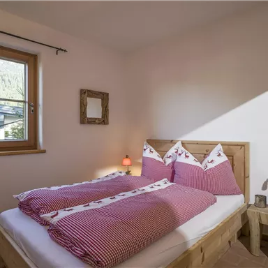 Ein gemütliches Schlafzimmer mit einem Holzbett und lila karierten Bettwäsche. Ein Fenster lässt natürliches Licht herein und schafft eine einladende Atmosphäre.