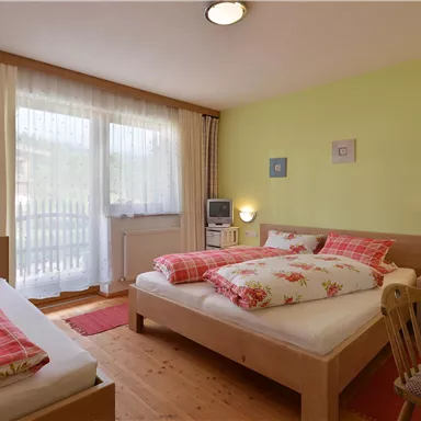 A cozy bedroom with two beds and bright colors. Large windows provide plenty of daylight.