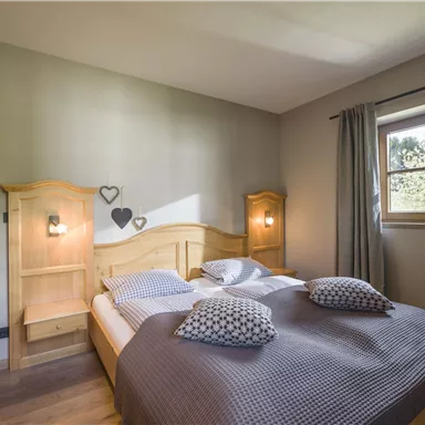 A cozy bedroom with a double bed and natural wood details. The room has windows with curtains and a warm, inviting atmosphere.