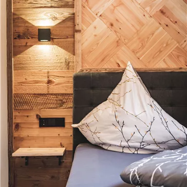 Ein modernes Schlafzimmer mit einem Holzwanddesign. Das Bett ist mit dekorativen Kissen ausgestattet und hat eine stilvolle Nachttischlampe.