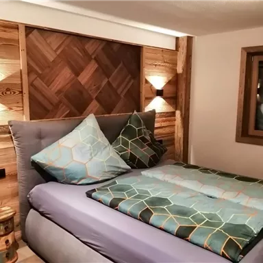 Ein gemütliches Schlafzimmer mit einem eleganten Bett und Holzverkleidung. Die Kissen und Bettdecke sind in ansprechenden Farben gestaltet.