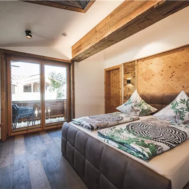 Ein gemütliches Schlafzimmer mit zwei Betten und bunten Kissen. Große Fenster bieten einen Blick auf einen Balkon und lassen viel Licht herein.