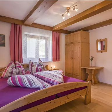 A cozy bedroom with a large double bed and colorful pillows. Wooden shelves and warm lighting create an inviting atmosphere.