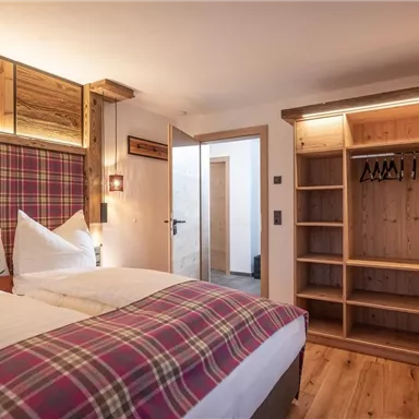 Ein gemütliches Schlafzimmer mit einem Doppelbett und einem modernen Holzmobiliar. Der Raum hat einen warmen, einladenden Charakter mit einer offenen Garderobe.