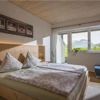 A bright and modern bedroom with a double bed and pictures on the wall. Large windows offer a view of the mountains and nature outside.
