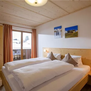 Ein gemütliches Schlafzimmer mit einem Doppelbett und hellem Holzinterieur. Große Fenster bieten einen Blick nach draußen und die Wände sind mit zwei Bildern dekoriert.