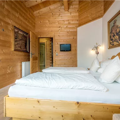 A cozy bedroom with wooden walls and two beds. A painting hangs on the wall, and there is a small television.