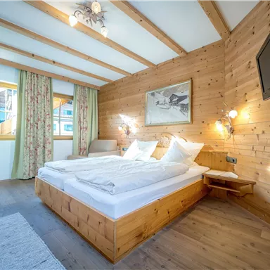 A cozy bedroom with wooden paneling and warm colors. It is bright and inviting, furnished with a double bed and a television.