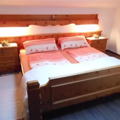 A cozy bedroom with a wooden bed and soft lighting. The bedding is in soft colors and there are nightstands on both sides.