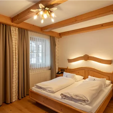 A cozy bedroom with a double bed and wood paneling. Large windows let in plenty of light, and there are beige curtains.