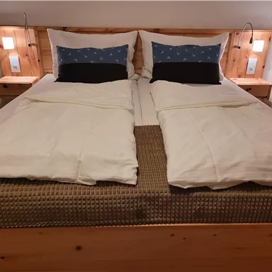 A cozy bedroom with a large bed and two pillows. The walls are light and there are night lights on the sides.