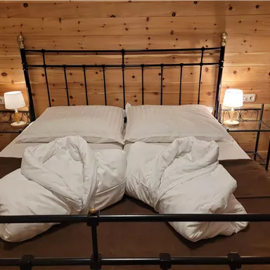 A cozy bedroom with a metal bed and two pillows. The wooden walls and soft lights create an inviting atmosphere.