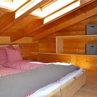 A cozy room with wooden paneling and two beds. There are shelves and boxes for storage, as well as skylights that provide natural light.
