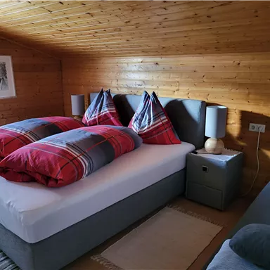 A cozy bedroom with a double bed and red cushions. The wooden ceilings and walls create a warm, inviting atmosphere.
