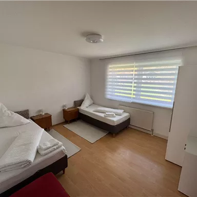A simple room with two single beds and minimalist decor. There is a bright wooden floor and plenty of natural light coming through the window.