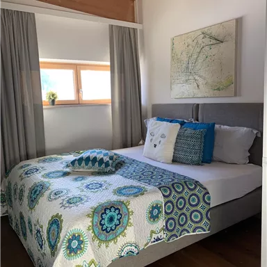 Ein gemütliches Schlafzimmer mit einem Doppelbett und bunten Kissen. Die Wände sind hell, und ein Fenster sorgt für ausreichend Tageslicht.