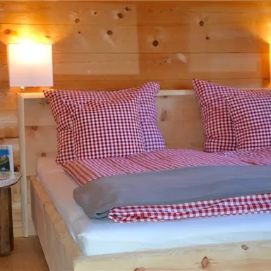 A cozy bedroom with a double bed and checkered pillows. The walls are made of wood, and soft lighting creates a warm atmosphere.