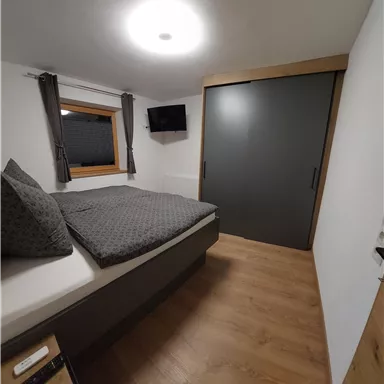 Ein modernes Schlafzimmer mit einem großen Bett und grauer Bettwäsche. Der Raum verfügt über einen Fernseher und einen Einbauschrank.