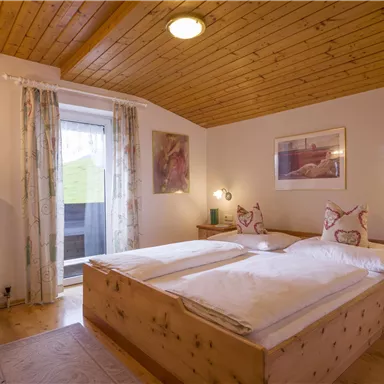 Ein gemütliches Schlafzimmer mit zwei Einzelbetten und Holzmöbeln. Große Fenster lassen viel Licht herein und bieten Zugang zu einem Balkon.
