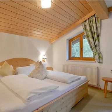 Ein gemütliches Schlafzimmer mit einem Doppelbett aus Holz und sanftem Licht. Die Wände sind hell, und das Zimmer hat große Fenster mit Blick nach draußen.