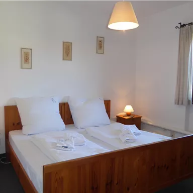 Ein gemütliches Schlafzimmer mit einem Doppelbett und Holzlatten. Der Raum ist hell und freundlich gestaltet, mit einem Fenster und Nachtlichtern.