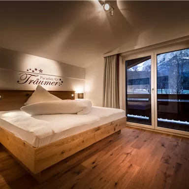 Ein gemütliches Schlafzimmer mit einem modernen Holzbett und einer Aussicht auf den Balkon. Die warmen Farben und die weichen Linien schaffen eine einladende Atmosphäre.