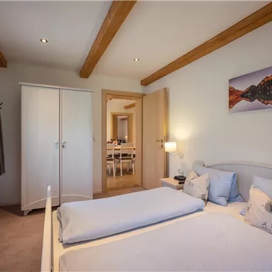 A cozy bedroom with a double bed and light-colored walls. The room contains a wardrobe and a picture on the wall.