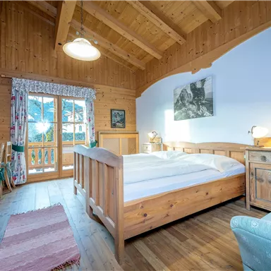 A cozy room with wooden ceilings and a large bed. There is a table and chairs as well as a small balcony with a view outside.