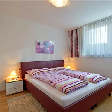 A cozy bedroom with a double bed and white bedding. The room has large windows that let in a lot of light.
