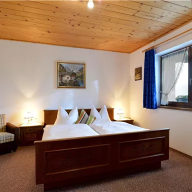 A cozy room with two beds and a wooden ceiling. The windows are decorated with blue curtains.