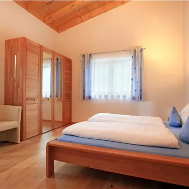 A bright and cozy bedroom with wooden furniture. The room features a double bed, a nightstand, and a wardrobe.