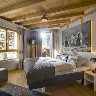 Ein modernes Schlafzimmer mit einem großen Bett und Holzdetails. Große Fenster bringen viel Tageslicht in den Raum.