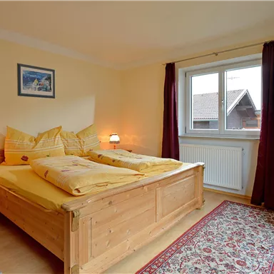A cozy bedroom with a double bed and two nightstands. It has light-colored walls, a window with curtains, and a television.