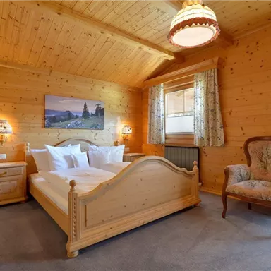A cozy bedroom with wooden walls and a large bed. Curtains hang at the windows, and there is a comfortable armchair.