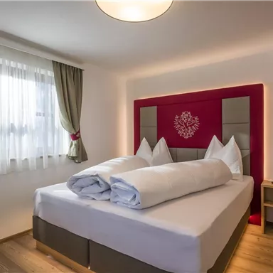 A cozy bedroom with a large bed and modern pillows. Large windows let in plenty of light, and the walls are painted in neutral colors.