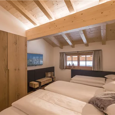 Ein gemütliches Schlafzimmer mit Holzdecken und drei Einzelbetten. Die Einrichtung ist modern und bietet einen Blick aus dem Fenster.