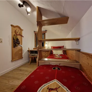 A cozy room with a wooden loft bed. The walls are light, and the bedding is red with a traditional pattern.
