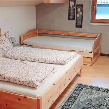 Ein gemütliches Schlafzimmer mit zwei Holzbetten und einem zusätzlichen Schlafplatz. Der Raum ist hell und wirkt einladend.