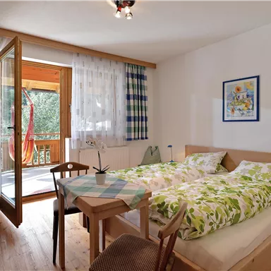 A cozy bedroom with a double bed and wooden floor. The door leads to a balcony with an outdoor view.